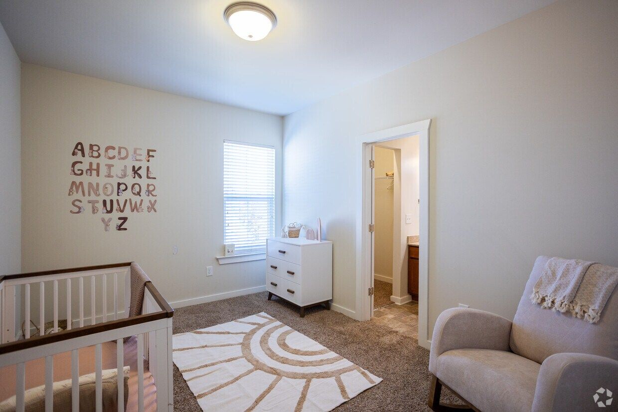 Bedroom staged as a nursery with a crib and armchair